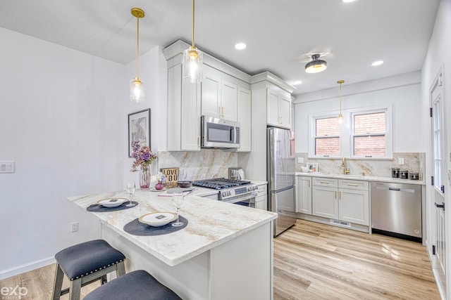 kitchen with decorative light fixtures, kitchen peninsula, a breakfast bar area, and appliances with stainless steel finishes