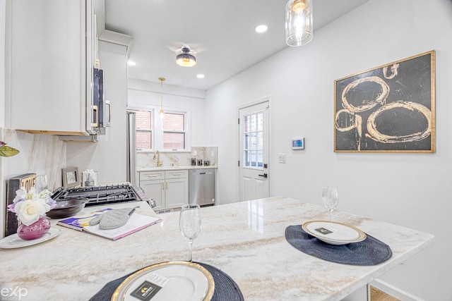 kitchen featuring white cabinetry, hanging light fixtures, tasteful backsplash, light stone counters, and appliances with stainless steel finishes