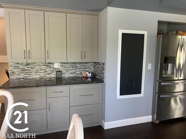 kitchen featuring dark hardwood / wood-style floors, stainless steel fridge with ice dispenser, backsplash, and dark stone counters