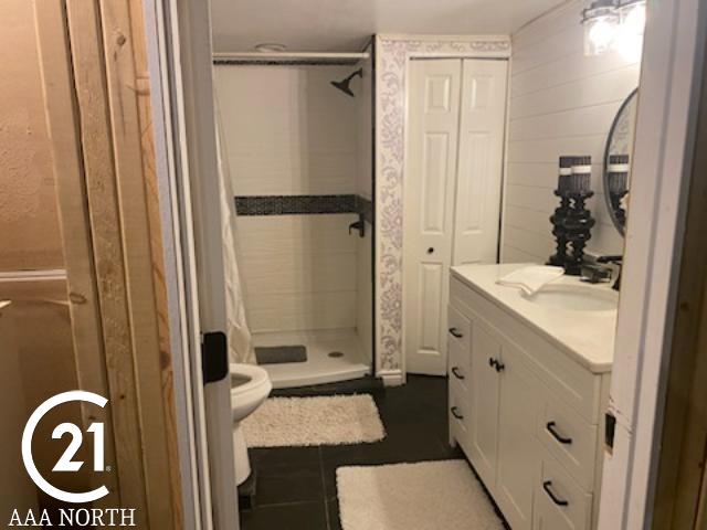 bathroom with a shower, tile patterned flooring, vanity, and toilet