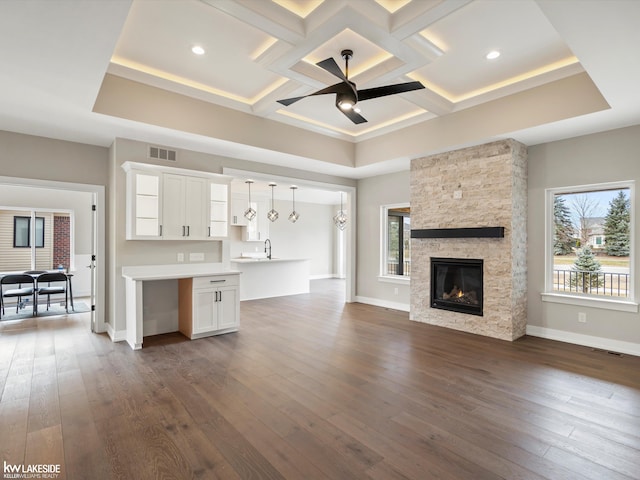 unfurnished living room featuring coffered ceiling, dark wood finished floors, visible vents, and a healthy amount of sunlight