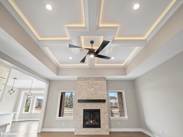 unfurnished living room with wood finished floors, coffered ceiling, a ceiling fan, and a stone fireplace