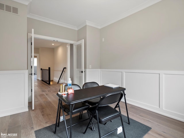 home office with a decorative wall, wood finished floors, visible vents, wainscoting, and crown molding