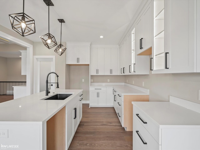 kitchen featuring pendant lighting, a center island with sink, white cabinetry, a sink, and wood finished floors