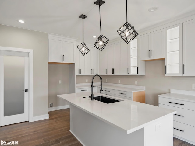 kitchen with dark wood-style floors, a center island with sink, hanging light fixtures, white cabinetry, and a sink