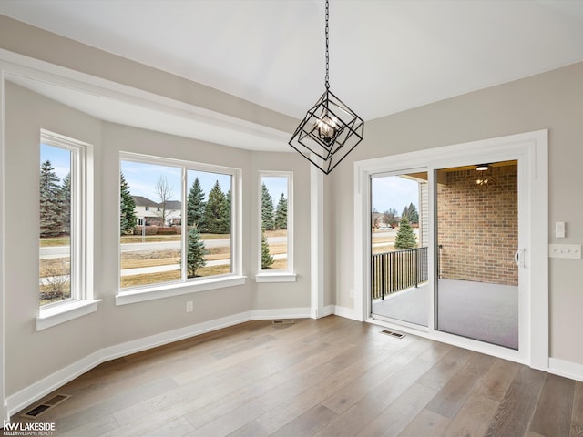 unfurnished dining area with an inviting chandelier, wood finished floors, visible vents, and baseboards