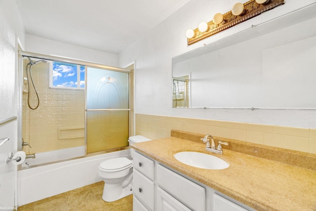 full bathroom with vanity, shower / bath combination with glass door, tile patterned flooring, toilet, and tile walls