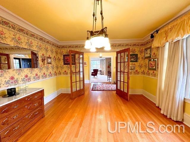 unfurnished dining area featuring wood-type flooring, french doors, and ornamental molding