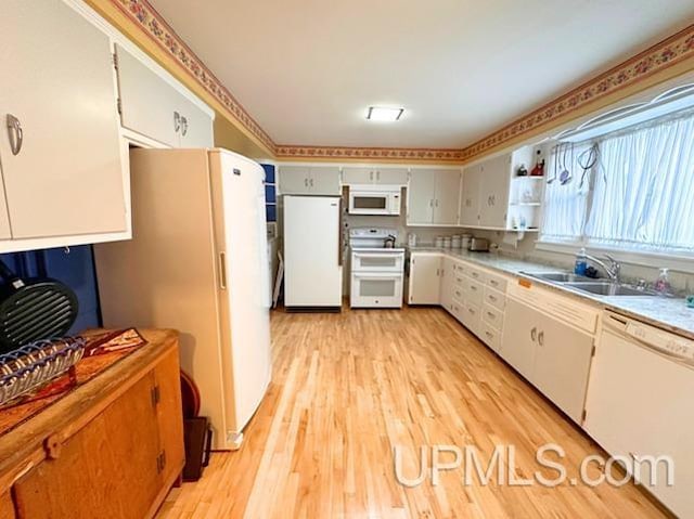 kitchen with white cabinets, light wood-type flooring, white appliances, and sink