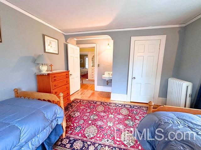 bedroom featuring light wood-type flooring, radiator heating unit, and crown molding