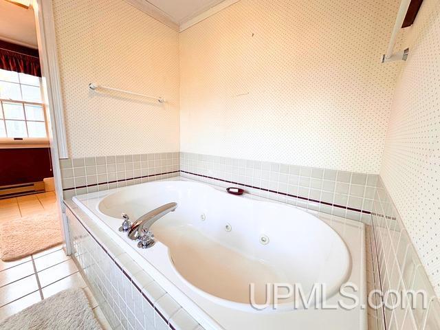 bathroom with tile patterned floors, ornamental molding, tiled bath, and a baseboard heating unit