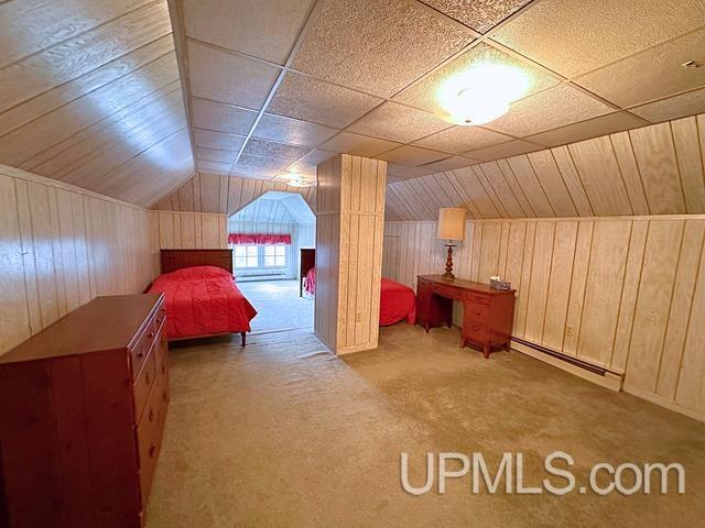 unfurnished bedroom with baseboard heating, wooden walls, carpet, and lofted ceiling