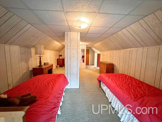 carpeted bedroom with wooden walls and vaulted ceiling