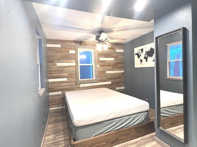 bedroom with ceiling fan, dark wood-type flooring, and wooden walls