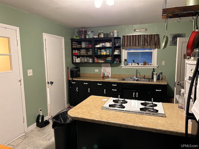 kitchen featuring dark cabinets, white stovetop, a sink, visible vents, and baseboards