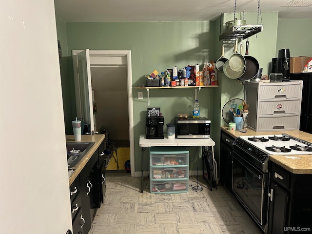 kitchen featuring gas range, stainless steel microwave, light countertops, dark cabinetry, and a sink