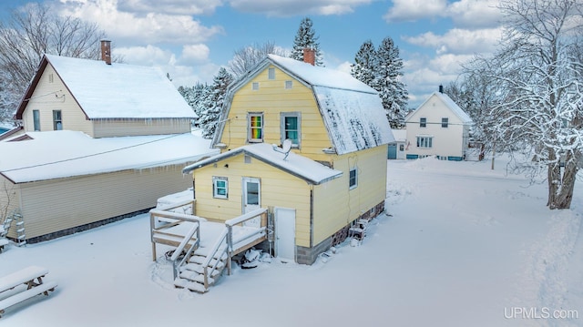 snow covered house with a chimney and a gambrel roof