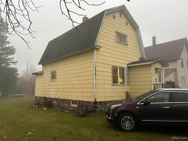 view of home's exterior with a shingled roof, a yard, a chimney, and a gambrel roof