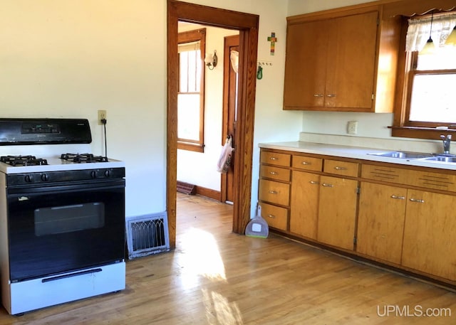 kitchen featuring light hardwood / wood-style floors, plenty of natural light, white gas range, and sink