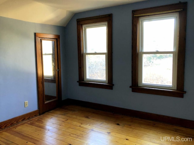 empty room with vaulted ceiling, hardwood / wood-style floors, and plenty of natural light