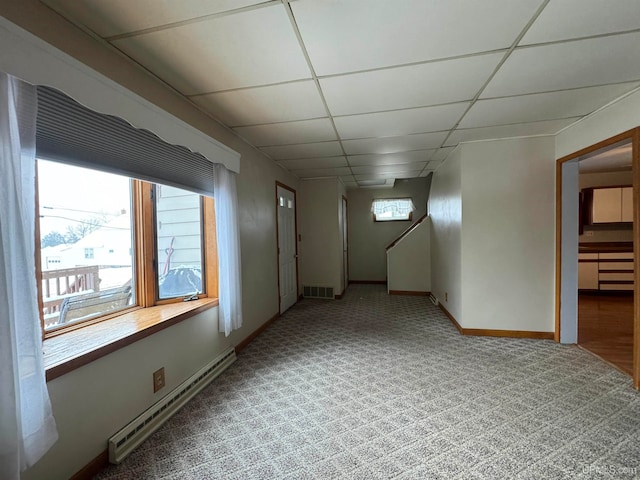 empty room featuring a drop ceiling, carpet, and a baseboard heating unit