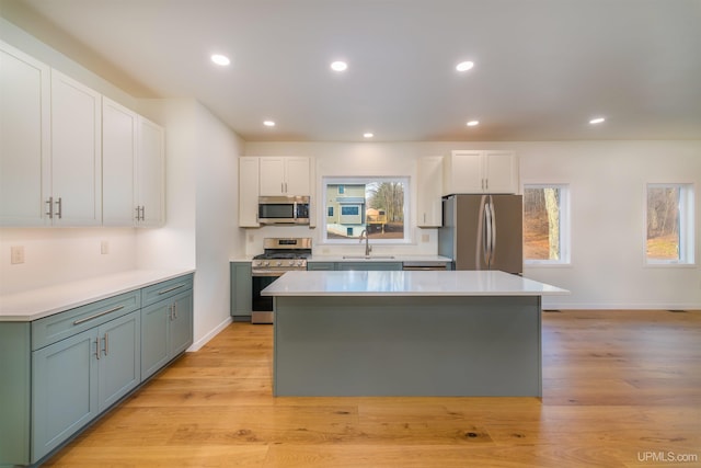 kitchen with white cabinets, stainless steel appliances, a wealth of natural light, and light hardwood / wood-style flooring