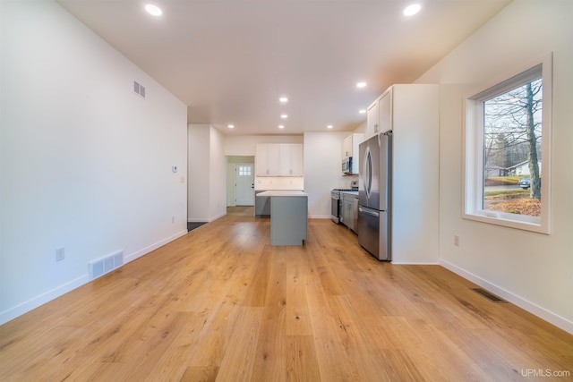 kitchen with white cabinets, stainless steel appliances, light wood-type flooring, and a kitchen island