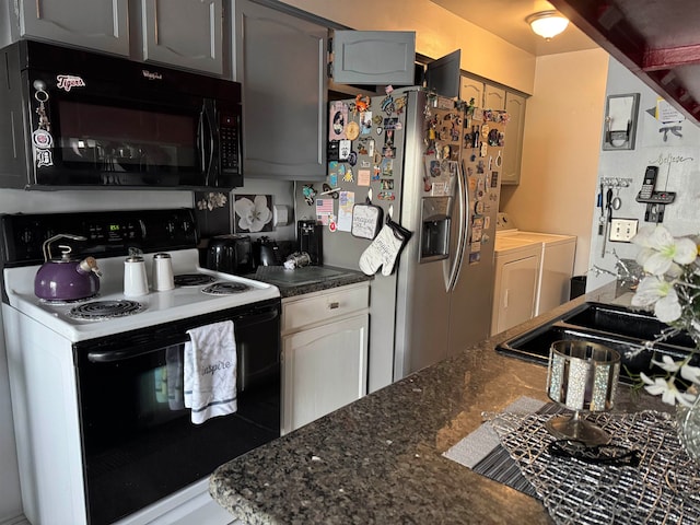 kitchen featuring dark stone counters, electric range, stainless steel fridge, gray cabinets, and washing machine and clothes dryer