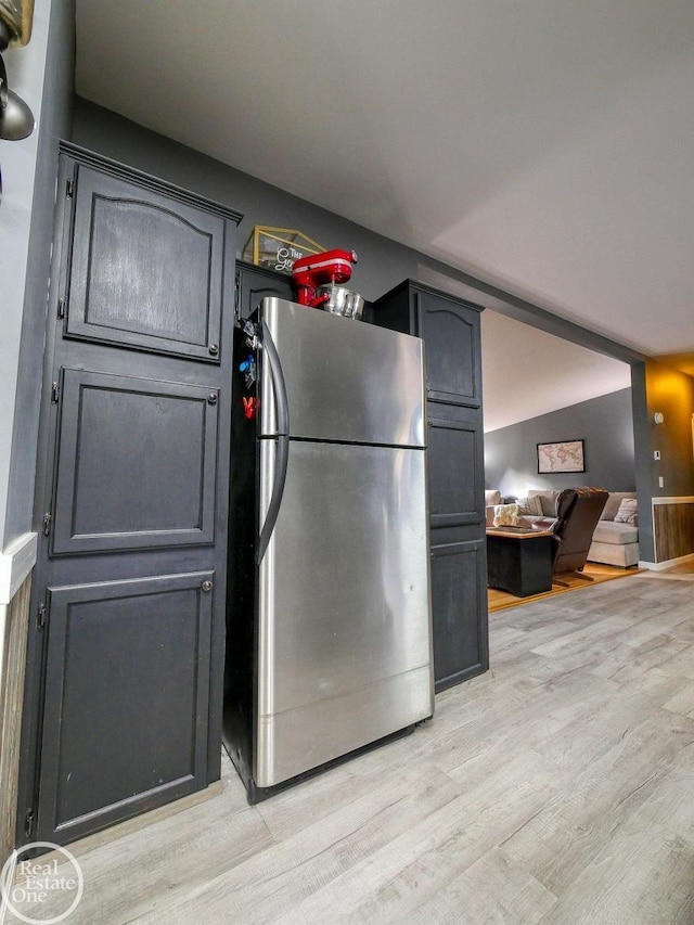 kitchen with stainless steel fridge, light hardwood / wood-style floors, and vaulted ceiling