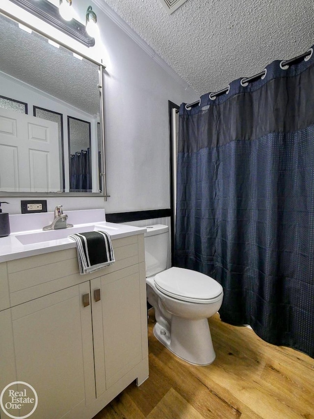 bathroom featuring vanity, a textured ceiling, crown molding, hardwood / wood-style flooring, and toilet