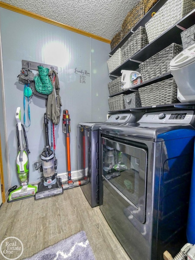 washroom with hardwood / wood-style flooring, washer and dryer, a textured ceiling, and ornamental molding