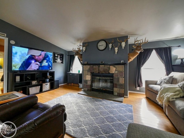 living room featuring wood-type flooring, a stone fireplace, and lofted ceiling