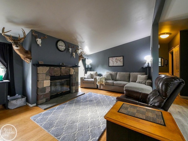 living room with light hardwood / wood-style floors, a stone fireplace, and lofted ceiling