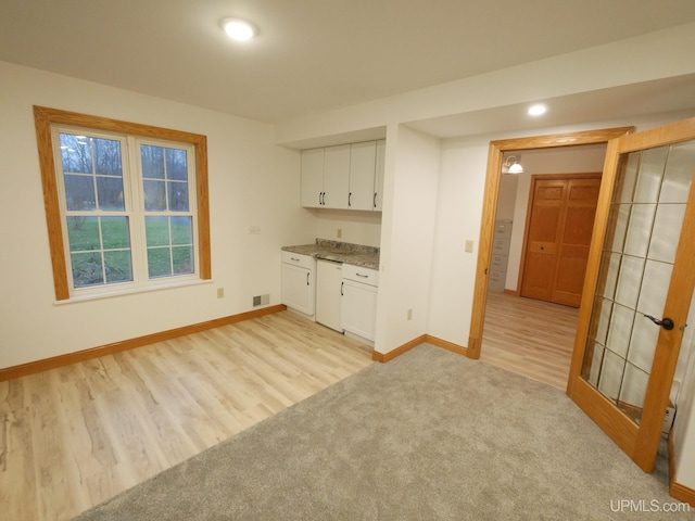 interior space featuring light wood-type flooring, white dishwasher, white cabinetry, and light stone counters