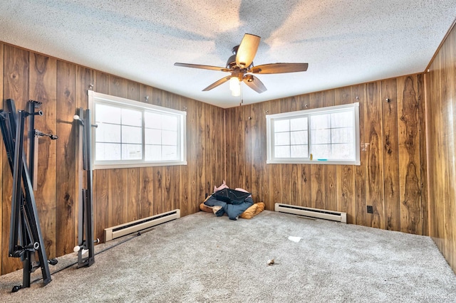 carpeted spare room featuring a textured ceiling, a baseboard radiator, ceiling fan, and wooden walls