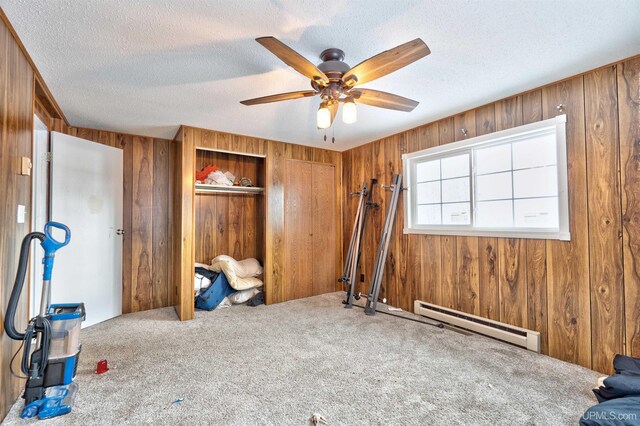 interior space with ceiling fan, a baseboard radiator, carpet floors, a textured ceiling, and wooden walls