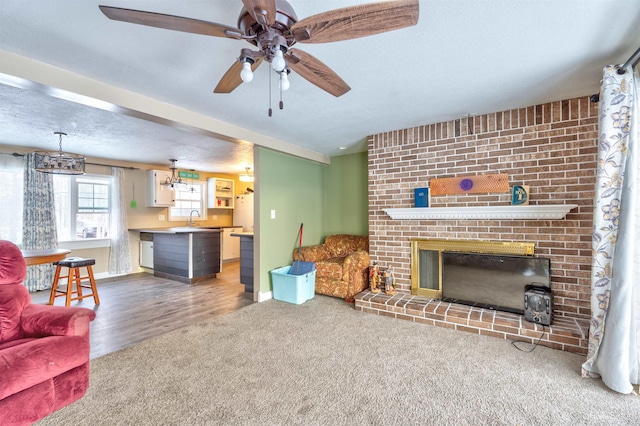 living room with sink, a brick fireplace, hardwood / wood-style flooring, ceiling fan, and a textured ceiling