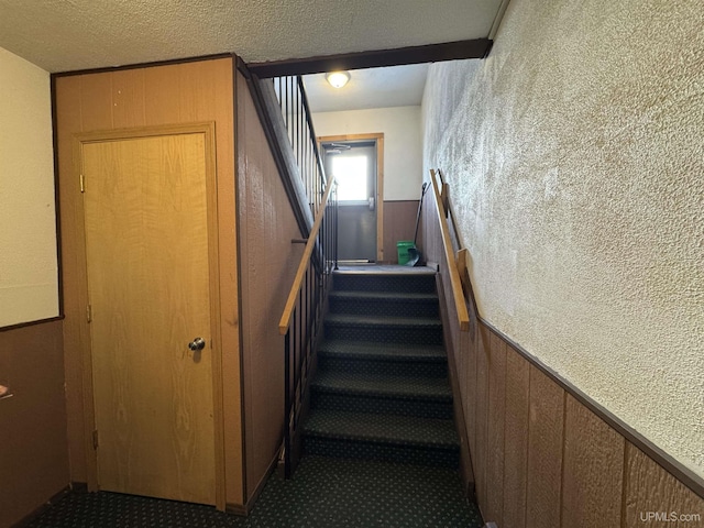 stairs with carpet, a textured ceiling, and wooden walls