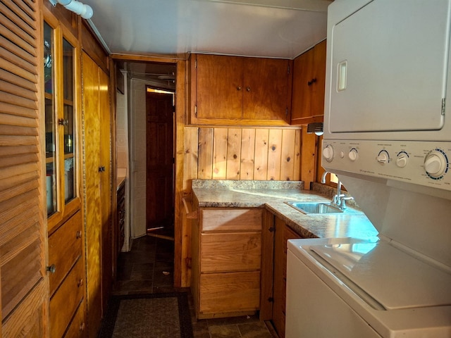 laundry area with dark tile patterned floors, stacked washer and clothes dryer, and sink