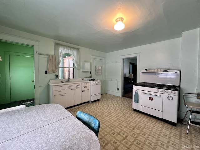 kitchen with white stove, white cabinetry, white range with gas cooktop, and sink