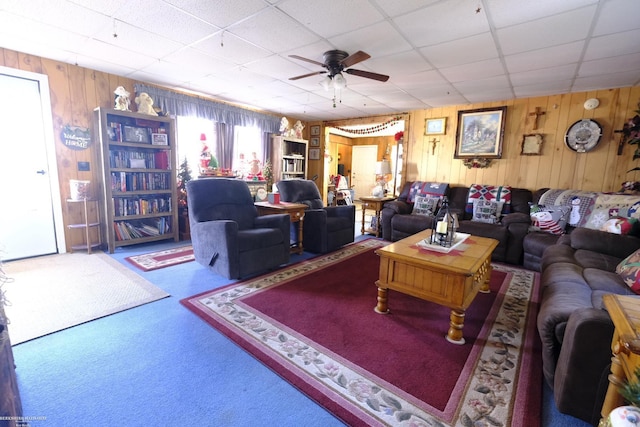 carpeted living room with a paneled ceiling, ceiling fan, and wood walls