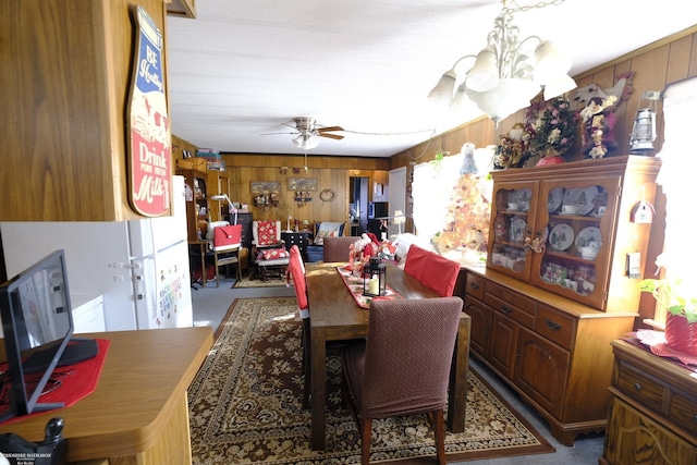 dining area with ceiling fan with notable chandelier, dark carpet, and wooden walls