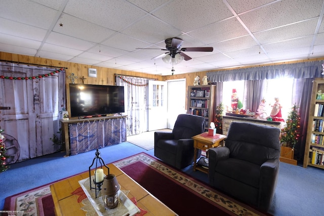 carpeted living room featuring a drop ceiling, ceiling fan, and wooden walls