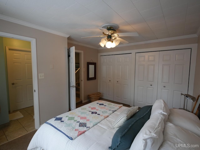 bedroom with tile patterned floors, ceiling fan, two closets, and ornamental molding