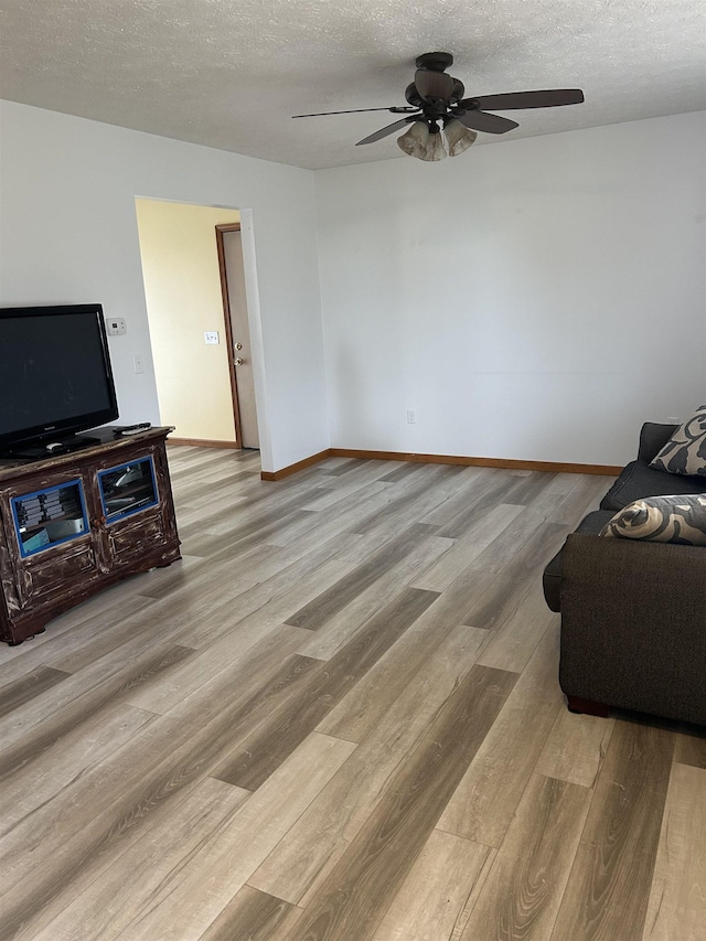 living room featuring ceiling fan, light hardwood / wood-style flooring, and a textured ceiling