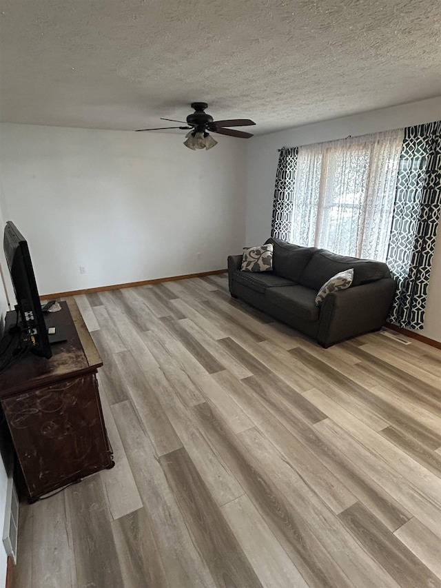 living room with ceiling fan, a textured ceiling, and light wood-type flooring