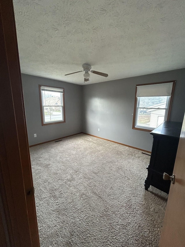 spare room featuring light colored carpet, ceiling fan, and a healthy amount of sunlight