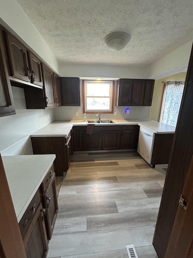 kitchen with dark brown cabinets, a textured ceiling, white dishwasher, sink, and light hardwood / wood-style floors