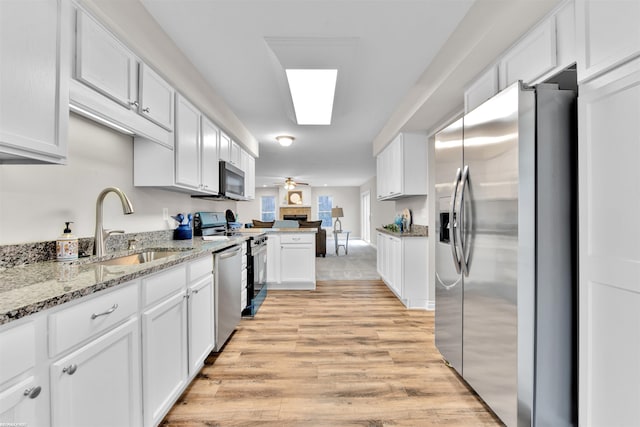 kitchen with white cabinetry, sink, light hardwood / wood-style flooring, kitchen peninsula, and appliances with stainless steel finishes