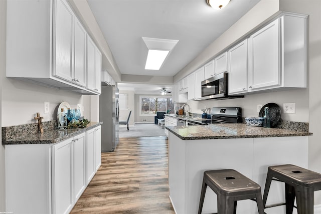 kitchen with kitchen peninsula, dark stone countertops, a breakfast bar area, white cabinets, and appliances with stainless steel finishes